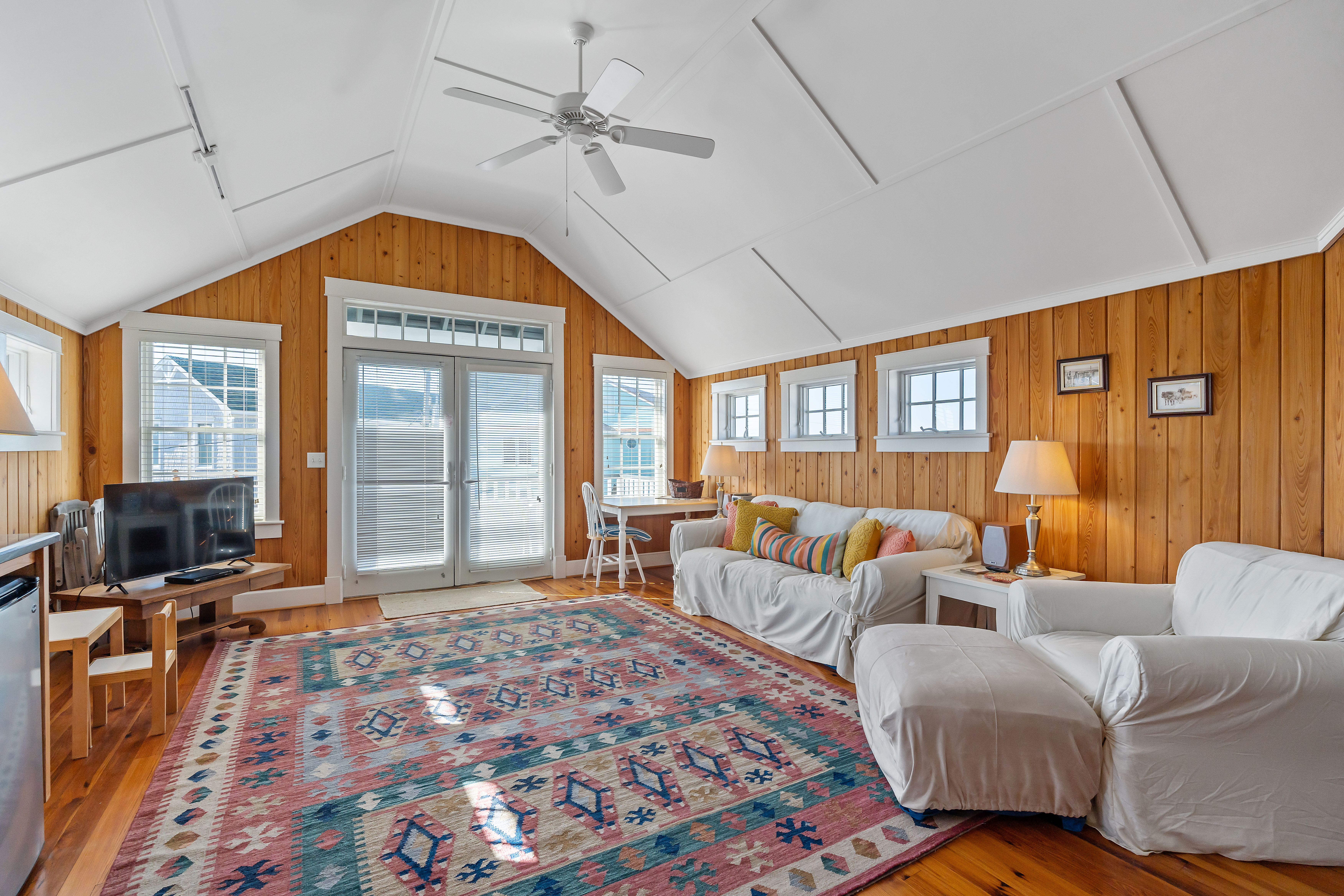 The pine-paneled common room under a vaulted white ceiling, doors open to the porch