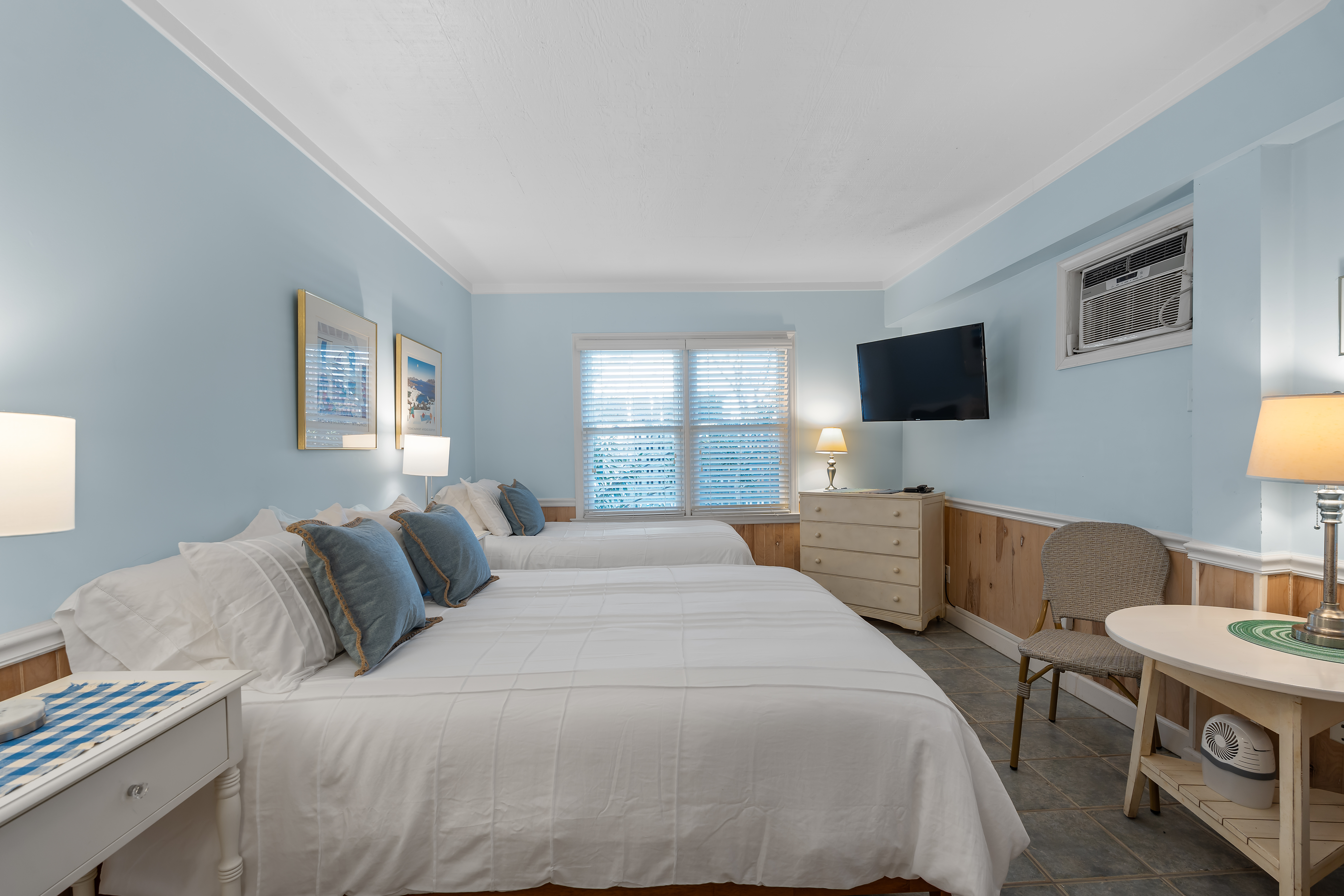 A pale blue bedroom with two beds made up in white